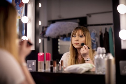 A young person applies make-up while looking into a mirror
