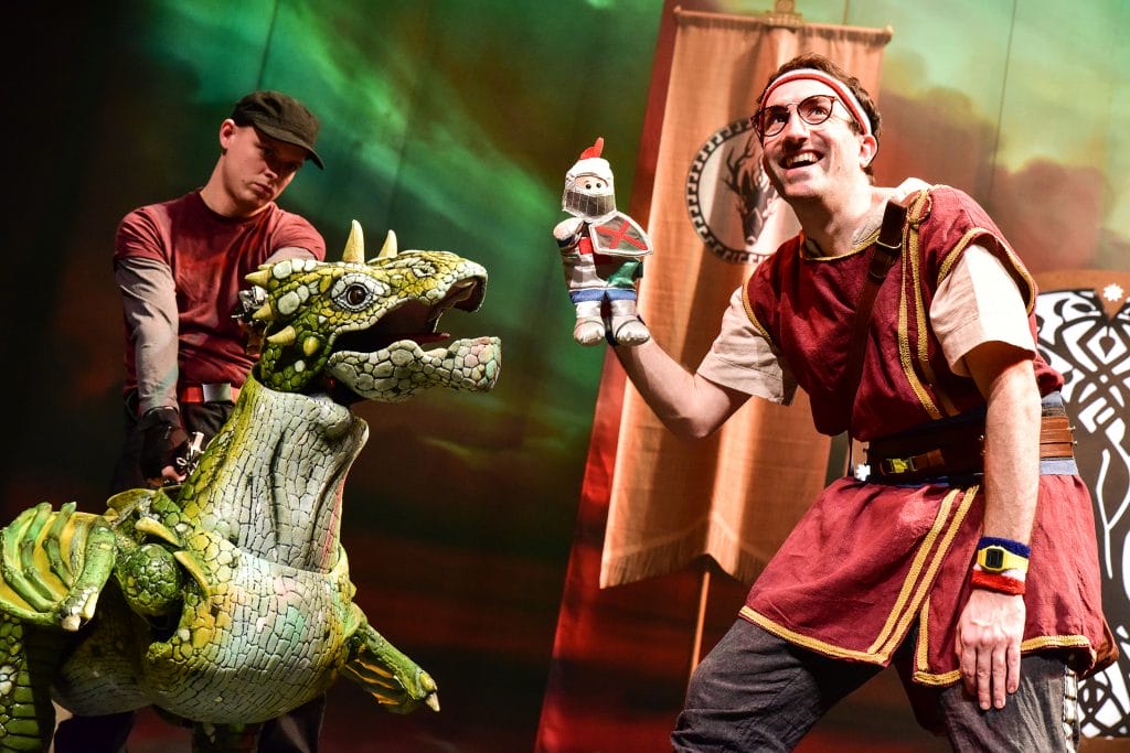 Photo of a man holding a knight doll with a dragon puppet