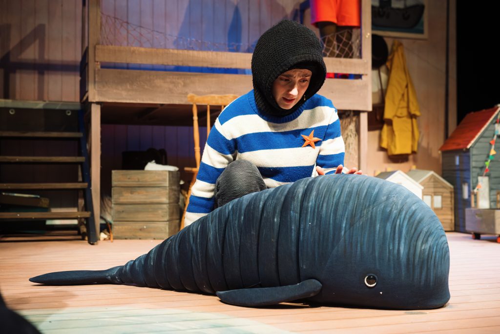 Production photo of Noi kneeling next to the whale touching its back