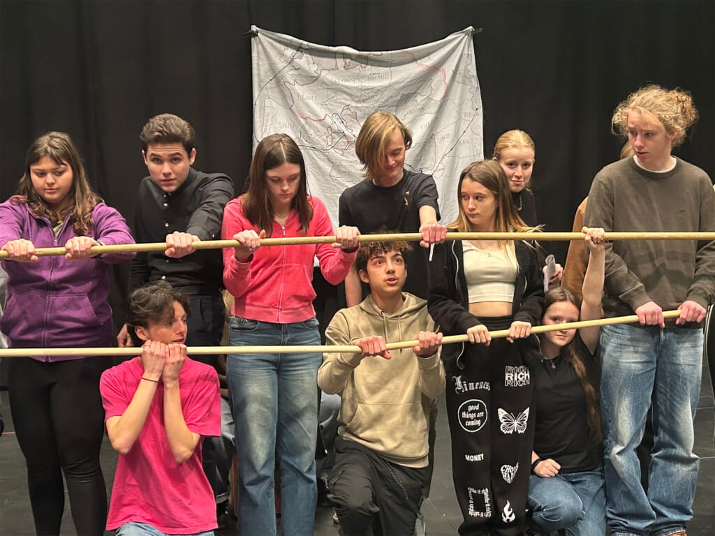 A group of children stand behind and hold onto two horizontal bars.