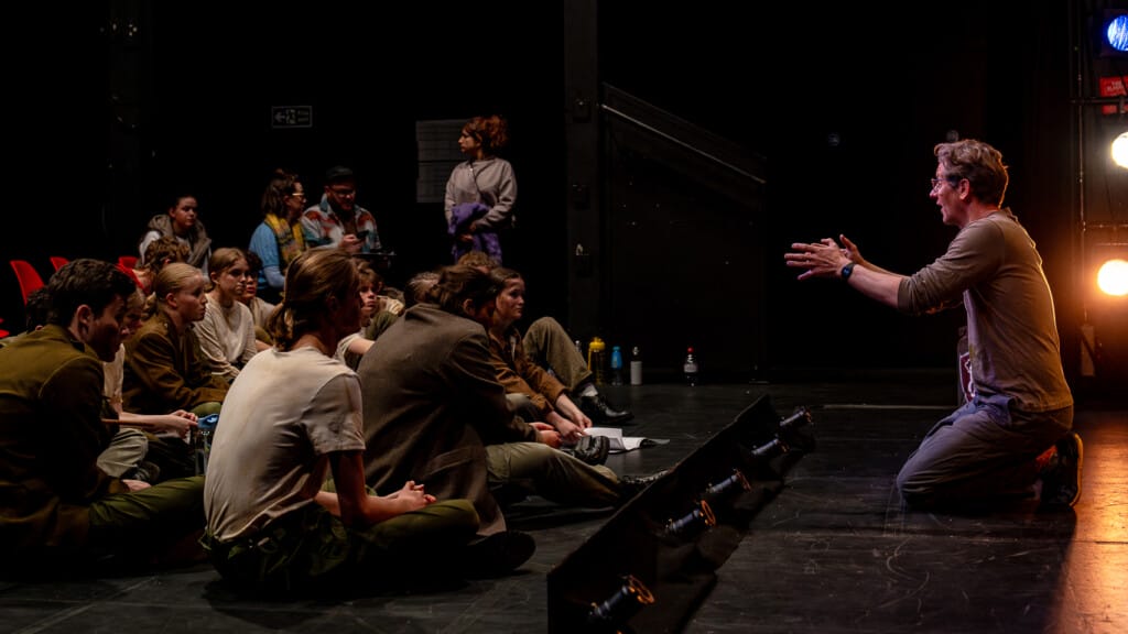 Writer Glenn Tillin directs the cast of Wojtek. He is knelt on the stage, and the cast are sat on the floor.